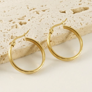 Macro shot of 18K gold twist earrings on beige textured stone background