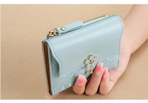 Close-up of light blue quilted short wallet with gold zipper and flower charm pendant