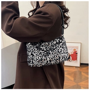 Detail of black sequined baguette bag with shoulder strap knot decoration on model