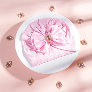 Close-up of pink baby turban hat with oversized bow and rhinestone jewel center