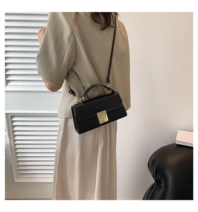 Detail of black leather crossbody bag featuring an elegant gold metal square lock closure