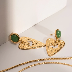 Dettaglio di orecchini a cuore vintage con metallo martellato oro e pietre verdi