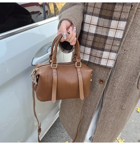 Detail view of brown pleated Boston bag with gold hardware and long shoulder strap