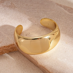 Close-up of a wide polished gold cuff bracelet resting on a textured stone block