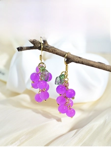 Detail of purple grape drop earrings with green leaves hanging on a natural branch