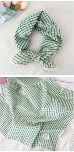 Macro detail of green gingham scarf featuring delicate white lace edges and linen texture