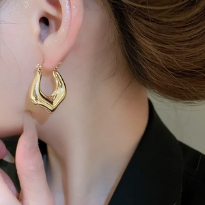 Detail of chunky golden hoop earring with sleek wavy texture on woman's ear