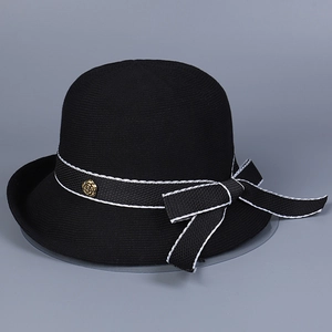 Detail of black knit cloche hat with ribbon bow and gold camellia metal badge