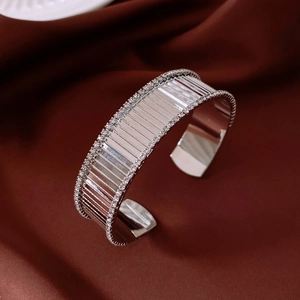Dettaglio del bracciale aperto argentato con cristalli su sfondo in raso di lusso