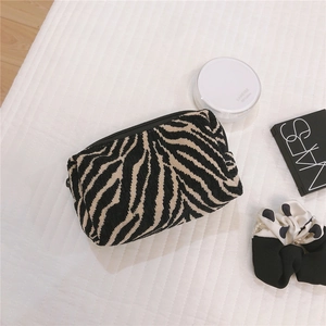 Macro detail of zebra pattern knit makeup bag with black zipper on quilted background