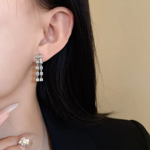 Close-up of elegant double-row square zircon tassel earrings on model with black blazer