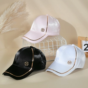 Détail de casquettes en satin rose, noir et blanc avec logo métallique M doré