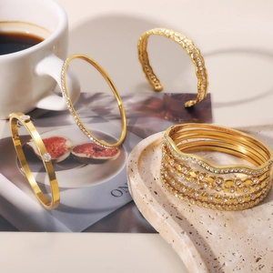 Dettaglio di bracciali in acciaio inossidabile dorato con zirconi incastonati e texture varie