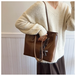 Brown leather tote bag with white stitching and cute cat charm on model shoulder