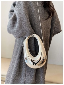 Silver metallic oval clutch bag with cutout handle and chain strap shown on a model
