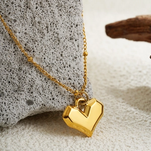 Polished 18K gold heart pendant necklace displayed on natural grey stone background