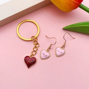 Gold keychain with red glitter heart and rose gold Love earrings on pink background
