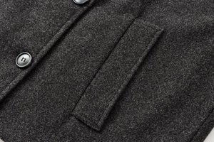 Dettaglio di un cappotto di lana grigio scuro con bottone e cuciture delle tasche curate