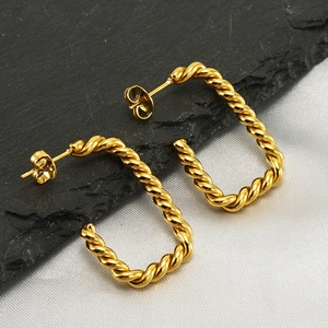 Macro shot of gold rectangular twisted hoop earrings on stone with high metal gloss