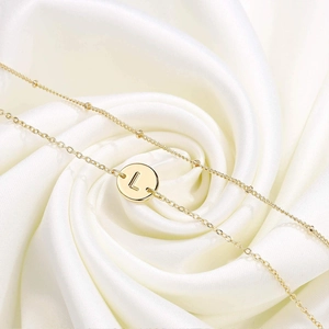 Détail d'un collier doré à deux rangs avec pendentif lettre L sur soie blanche douce