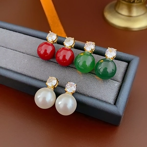 Gros plan de boucles d'oreilles dorées avec zircons et perles en rouge, vert et blanc