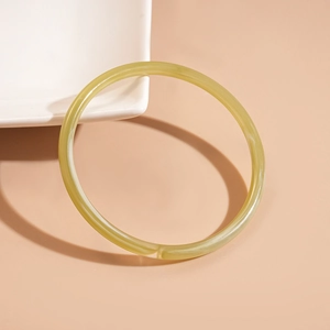 Macro detail of a translucent pale yellow acrylic round bangle on a white ceramic tray