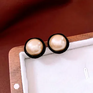 Elegant champagne pearl earrings with black velvet trim in a wooden jewelry display case