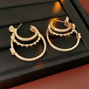Close-up of gold three-layer circular earrings with cubic zirconia on black leather box