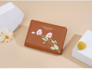 Detail of a brown short wallet with pink floral embroidery and golden metal frame edge
