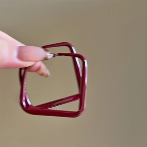 Detailed close-up of dark red geometric square earrings held for scale comparison