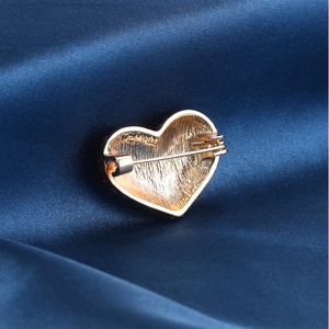 Macro detail of gold heart brooch back showing brushed metal texture and safety pin clasp