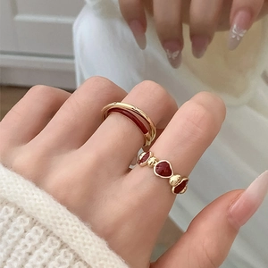 Detail view of stacked gold rings with red enamel flowers and heart on a hand