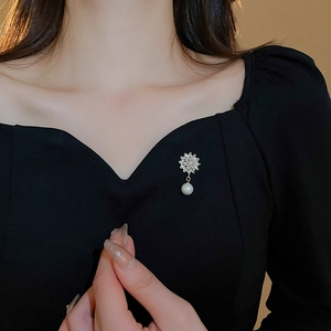 Macro detail of gold-plated flower brooch with pavé zircon crystals and hanging white pearl