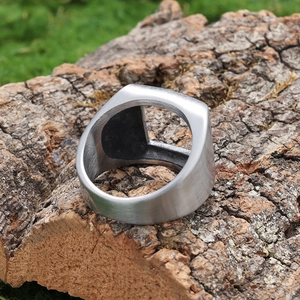 Détail d'une bague large en acier inoxydable brossé avec découpe sur base en bois