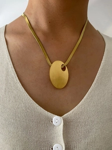 Detailed view of a gold snake chain necklace with an oval pendant on a model's neck