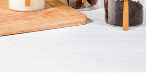 Macro shot of glass spice jars with bamboo lids and spoons on a white wooden table