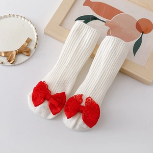 Detail of white ribbed baby socks with oversized red lace bows on the toes
