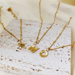 Detailed view of three gold titanium necklaces with textured letter pendants on stone