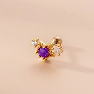 Detalle de piercing dorado con piedra redonda púrpura y acentos en forma de estrella