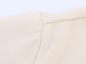 Close-up of the textured beige cotton-linen fabric and clean stitching on the shirt shoulder
