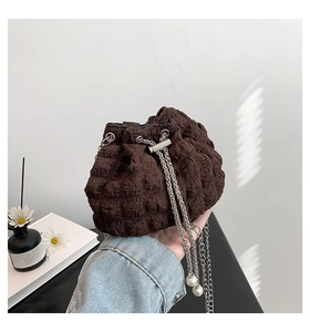 Detailed shot of brown pleated bucket bag featuring silver chain and pearl charm