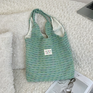 Close-up of a colorful hand-woven knit tote bag with brand label on a plush rug