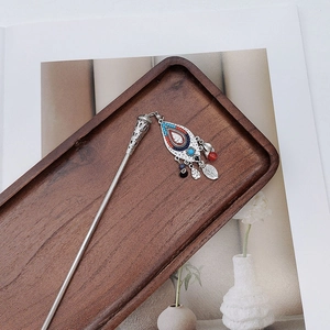 Detail of silver ethnic hair pin with colorful enamel charms on a dark wooden tray
