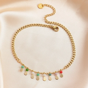 Detail of a gold chain anklet with multicolor droplets on a beige silk fabric background