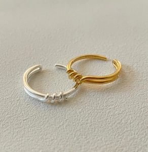 Detailed view of silver and gold knotted twist rings on a soft textured background