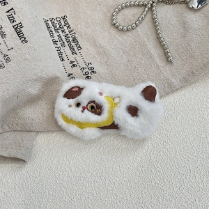 Detailed close-up of a plush white cat brooch pin with brown ears on linen background