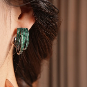Close-up of multi-layer C-shaped earrings with green zircon on model for an elegant look
