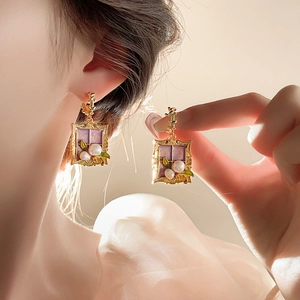 Detail of vintage gold flower earrings with purple enamel and white pearls worn by a model