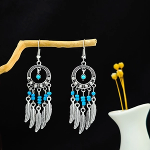 Détail de boucles d'oreilles bohèmes argentées avec perles bleues et plumes sur bois