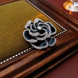 Detail of a black enamel camellia flower brooch with rhinestones on a vintage wooden base